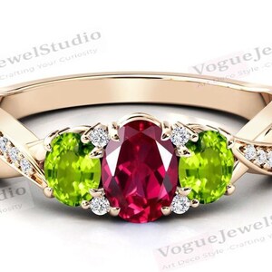 May include: A gold ring featuring a red oval gemstone, flanked by two green oval gemstones. The ring is set with smaller diamonds around the gemstones.