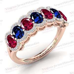 Può includere: Un anello con fascia in oro con una fila di pietre ovali rosse e blu alternate circondate da pietre più piccole e trasparenti.