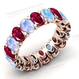 May include: A rose gold eternity band ring with alternating oval-shaped red ruby and white moonstone gemstones.