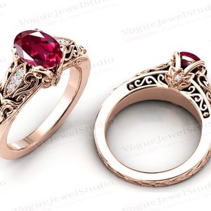 May include: A rose gold engagement ring with an oval-shaped ruby gemstone and diamond accents. The ring features a delicate, intricate filigree design.