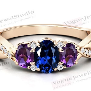 May include: A rose gold ring with a twisted band set with three oval-shaped gemstones. The center stone is a deep blue sapphire, flanked by two smaller amethyst stones. The band is accented with small round diamonds.