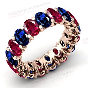May include: A gold band ring with alternating oval-shaped red and blue gemstones. The ring is set with a total of 12 gemstones.