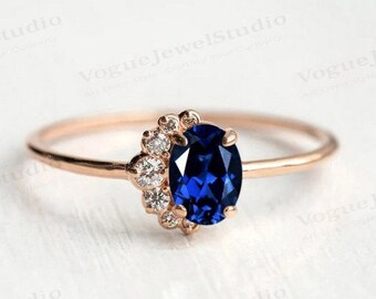 May include: A rose gold ring with a large oval blue sapphire gemstone surrounded by a halo of smaller white diamonds.