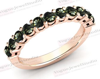 Op de afbeelding: Een roségouden bandring met een rij groene edelstenen. De ring is bezet met ronde, gefacetteerde stenen die gelijkmatig over de band zijn verdeeld.