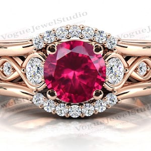 May include: A three-piece rose gold engagement ring set with a large oval ruby centre stone surrounded by a halo of smaller diamonds. The band features a delicate infinity design with additional diamonds.