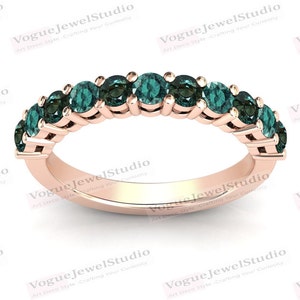 Puede incluir: Anillo de oro rosa con una fila de piedras preciosas de color verde azulado. El anillo tiene una banda delgada y está engastado con varias piedras redondas. Las piedras preciosas son de un color verde azulado intenso y el anillo se muestra sobre un fondo blanco.