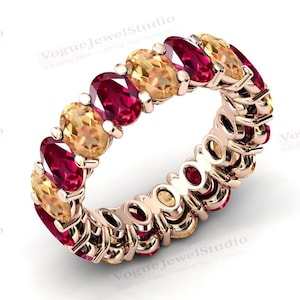 Puede incluir: Un anillo de banda de oro con piedras ovaladas rojas y amarillas alternas. El anillo está engastado con un total de 12 piedras.