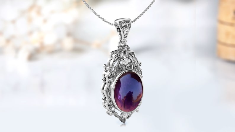 May include: A silver pendant necklace with an ornate design featuring a large oval-shaped purple gemstone surrounded by smaller clear gemstones.