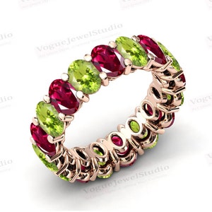 May include: A rose gold eternity band ring with alternating red ruby and green peridot gemstones.