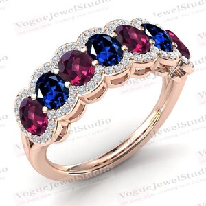 May include: A rose gold ring featuring alternating oval-cut gemstones in deep red and sapphire blue, each surrounded by a halo of small, sparkling diamonds. The ring's band is a delicate, polished metal.
