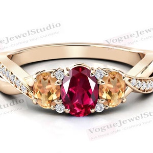 Könnte beinhalten: Ein goldener Ring mit einem roten ovalen Edelstein und zwei kleineren ovalen Topas-Edelsteinen. Der Ring ist mit kleinen Diamanten auf der Ringschiene besetzt.