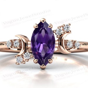 Könnte beinhalten: Roségoldener Ring mit einem marquiseförmigen, lila Amethyst-Mittelstein. Der Ring hat ein himmlisches Design mit Halbmond-Akzenten und kleinen, runden, klaren Edelsteinen. Das Band des Rings ist aus zartem, poliertem Roségold.