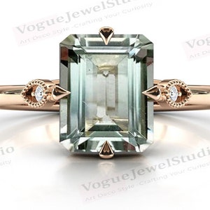 May include: A rose gold ring with a large emerald-cut green gemstone and two smaller round diamonds on the sides. The ring has a pointed design on the sides of the gemstone.