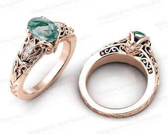May include: Rose gold ring featuring an oval moss agate gemstone and small accent diamonds. The ring has an ornate, filigree design with floral and scroll details. The band is engraved with a textured pattern. The ring is displayed from two angles.