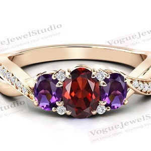 Op de afbeelding: Een gouden ring met een rode ovale edelsteen en twee paarse ovale edelstenen. De ring is bezet met kleine diamanten op de band.