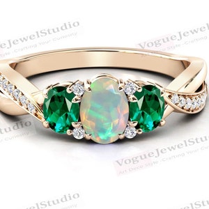May include: A gold ring with a white opal and two green emerald gemstones. The ring has a twisted band with small diamonds set in the band.