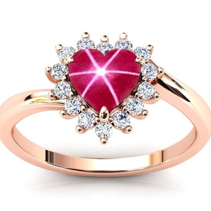 Op de afbeelding: Een hartvormige robijnring met een stervormig patroon en een halo van kleinere diamanten, gezet in roségoud.