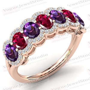 May include: A rose gold band ring with five oval-shaped gemstones. The gemstones alternate between deep purple and red. Each gemstone is surrounded by a halo of smaller, clear gemstones.
