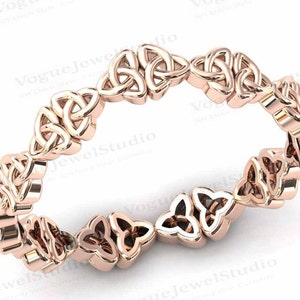 Puede incluir: Un anillo de eternidad de nudo celta de oro rosa. El anillo está formado por una serie de nudos entrelazados, cada uno con forma de trébol.