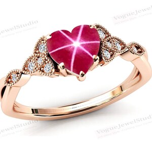 May include: A rose gold ring featuring a heart-shaped ruby gemstone with diamond accents. The ruby has a star-like pattern within it.