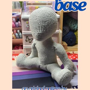 May include: A crocheted doll body base in light gray, with arms and legs extended. The image includes the text "no-sew! body base" and "an original pattern by KAMFOR". The background includes craft supplies.