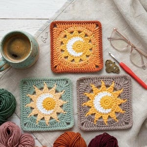 May include: Three crocheted square coasters with sun and moon designs in orange, green, and brown. A mug of coffee, yarn, glasses, and a crochet hook are also present. The coasters are handmade.