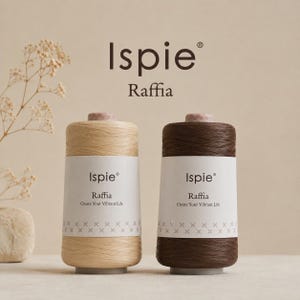 Puede incluir: Dos bobinas cilíndricas de hilo Ispie Raffia, una en color beige claro y otra en marrón oscuro. Cada bobina presenta una etiqueta de papel blanco con el texto Ispie Raffia Create Your Vibrant Life y una fila decorativa de pequeñas cruces.
