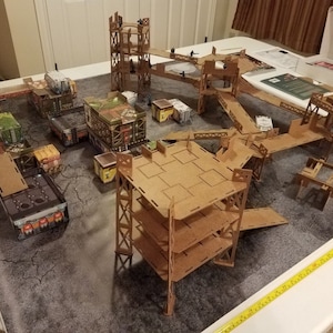 May include: A cardboard model of a futuristic city with multiple levels and walkways. The model is made of brown cardboard and has a gray and white textured surface. The model is set up on a table with a white surface.