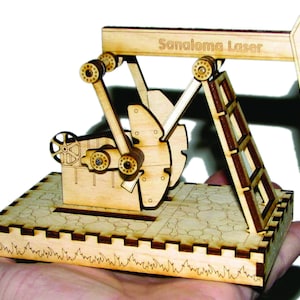 Könnte beinhalten: Ein Holzmodell eines Ölpumpenbockes mit einer Leiter und einem Sockel. Das Modell ist mit "Sanaloma Laser" beschriftet.