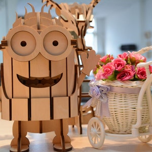 May include: Wooden laser-cut models of a cartoon character, a guitar, and a tricycle with a basket of pink roses. The character has large eyes and a smiling mouth. The tricycle is white, and the guitar is light brown.