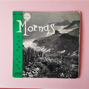 Pode incluir: Uma fotografia a preto e branco de uma paisagem montanhosa com uma praia em primeiro plano. A fotografia está numa capa de disco verde com o texto "Mornas de Cabo Verde" e "Valente 72" impresso nela.