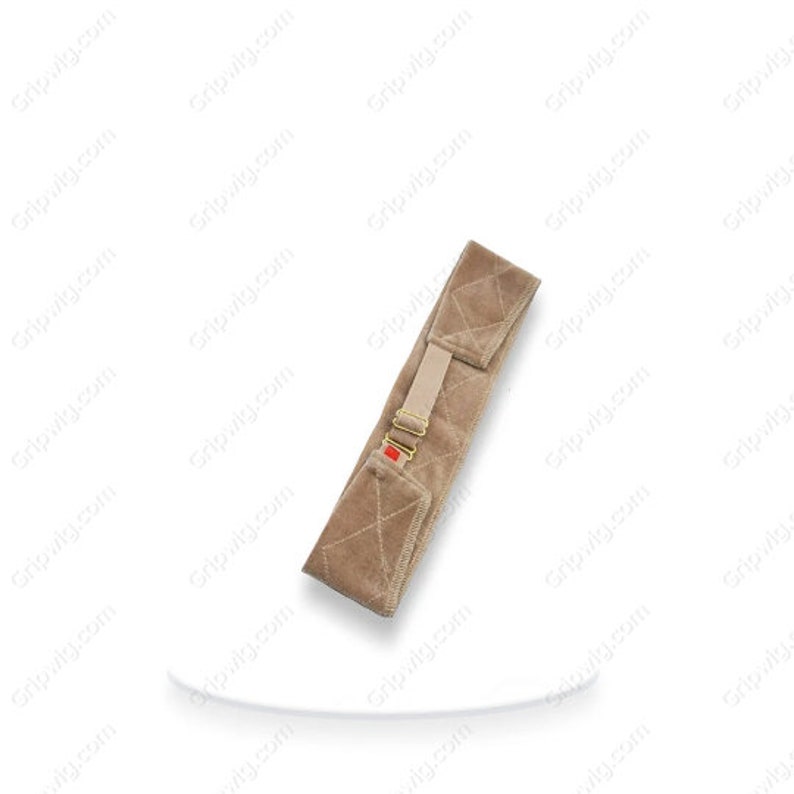 May include: A beige velvet wig grip with a gold buckle and a red tab. The grip is designed to help secure a wig in place.