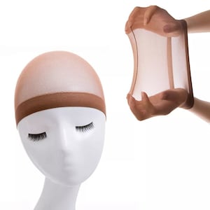 Può includere: Un cappuccio per parrucca color carne, realizzato in un materiale trasparente ed elastico. Il cappuccio è mostrato su una testa di manichino e anche tenuto in una mano, dimostrando la sua flessibilità.