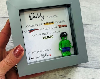 May include: A gray picture frame with a white card inside. The card has a message that reads "Daddy you are... as smart as Iron Man as kind as Superman as strong as Thor and as incredible as Hulk. I love you Daddy. Love your Bella." A green Lego Hulk figure is in the frame.