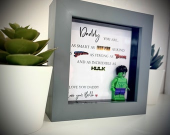 May include: A gray shadow box with a white background and a message that reads "Daddy you are... as smart as Iron Man as kind as Superman as strong as Thor and as incredible as Hulk. Love you Daddy. Love you Belk."  The box also features a Lego figurine of the Hulk.