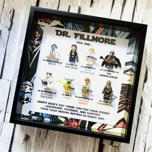 Peut inclure: Une œuvre d'art encadrée avec des figurines Lego Star Wars. Le cadre noir entoure un fond blanc avec le texte "DR. FILLMORE YOU ARE..." et des comparaisons de personnages. Comprend R2-D2, Han Solo, Luke Skywalker, The Mandalorian, un Stormtrooper, Yoda, Obi-Wan Kenobi et Chewbacca.