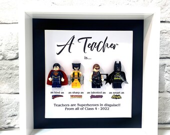 May include: A framed print with a white background and black border. The print features four Lego minifigures of superheroes, including Superman, Wolverine, Hawkeye, and Batman. The text reads "A Teacher is... as kind as Superman, as sharp as Wolverine, as talented as Hawkeye, as smart as Batman. Teachers are Superheroes in disguise!! From all of Class 4 - 2022."