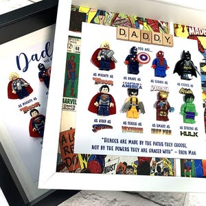 Può includere: Una cornice bianca con un collage di pagine di fumetti e minifigure Lego. La cornice ha la parola "DADDY" scritta con tessere di lettere. Il testo "You are..." è seguito da un elenco di tratti di supereroi, come "As mighty as Thor" e "As brave as Captain America". La citazione "Heroes are made by the paths they choose, not by the powers they are graced with - Iron Man" è stampata sotto l'elenco.