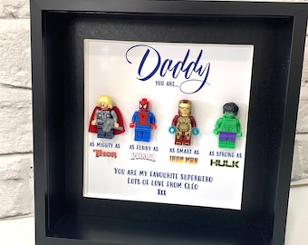 May include: A framed print with a white background and black frame. The print features four Lego minifigures of superheroes: Thor, Spiderman, Iron Man, and Hulk. The text reads "Daddy You Are... As Mighty As Thor, As Funny As Spiderman, As Smart As Iron Man, As Strong As Hulk. You Are My Favourite Superhero Lots Of Love From Cleo XXX."