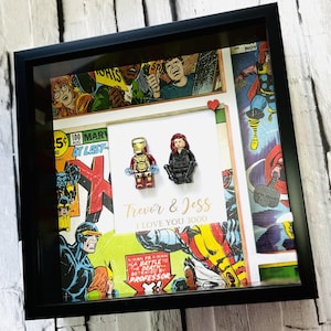 May include: Framed artwork with comic book panels and Lego figures of Iron Man and Black Widow. The artwork includes the text "Trevor & Jess I LOVE YOU 3000" and is enclosed in a black frame.