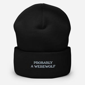 May include: Black beanie with the embroidered text "PROBABLY A WEREWOLF" in light gray. The beanie is made of a soft, knitted material and has a folded cuff. The hat is a winter accessory.