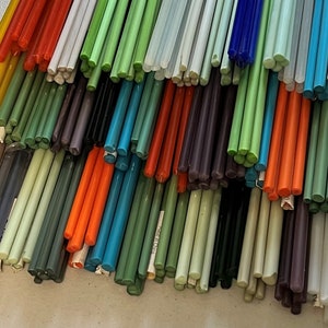 May include: A large collection of glass rods in various colours, including yellow, green, blue, orange, and purple. The rods are arranged in a pile, with the ends of the rods visible.