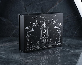 May include: A rectangular black box featuring silver foil illustrations of celestial motifs, including stars, a crescent moon, and an arched gateway. The text "WHAT'S PAST IS PROLOGUE" and Chinese characters are printed on the front surface.