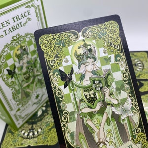 Może przedstawiać: Karta tarota z talii "Green Trace Tarot", z zieloną ilustracją ukoronowanej postaci trzymającej książkę i laskę z motylem. Karta ma czarną obw&oacute;dkę z zielonymi wzorami i tekstem "GREEN TRACE TAROT".