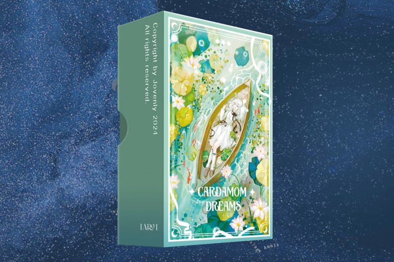 May include: A green box with the text "Cardamom Dreams" on the front. The box features an illustration of a boat with a person in it, surrounded by water lilies and other aquatic plants. The text "Copyright by Jovenly 2024" and "All rights reserved" are printed on the side of the box.