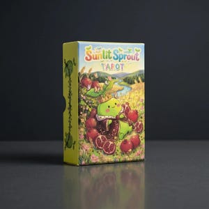 May include: A tarot card box with the text "Sunlit Sprout Tarot." The box features a cartoon illustration of a green sprout character wearing a crown and surrounded by pomegranates. The background shows a field, river, and butterflies.