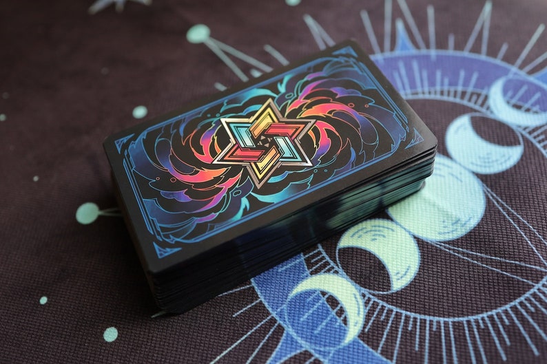 K&ouml;nnte beinhalten: Ein Kartenspiel mit schwarzem Hintergrund und einem farbenfrohen, geometrischen Design in der Mitte. Das Design zeigt eine Sternform mit mehreren Schichten und einem Regenbogen-Farbschema.