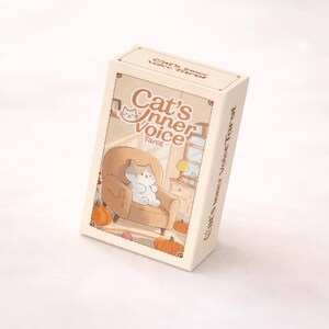 May include: A rectangular deck of Cat's Inner Voice Tarot cards in a cream-colored box. The box features an illustration of a cat sitting in a tan armchair surrounded by orange pumpkins, with the text Cat's Inner Voice Tarot printed on the front.