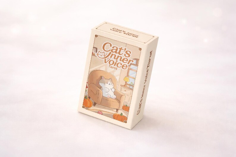May include: A rectangular deck of Cat's Inner Voice Tarot cards in a cream-colored box. The box features an illustration of a cat sitting in a tan armchair surrounded by orange pumpkins, with the text Cat's Inner Voice Tarot printed on the front.