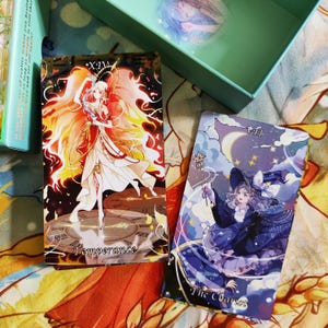 May include: Two tarot cards, one with a woman in a flowing white dress with orange flames around her, and the text "XIV Temperance". The other card features a woman in a blue dress and a witch's hat, with the text "VII The Chariot".